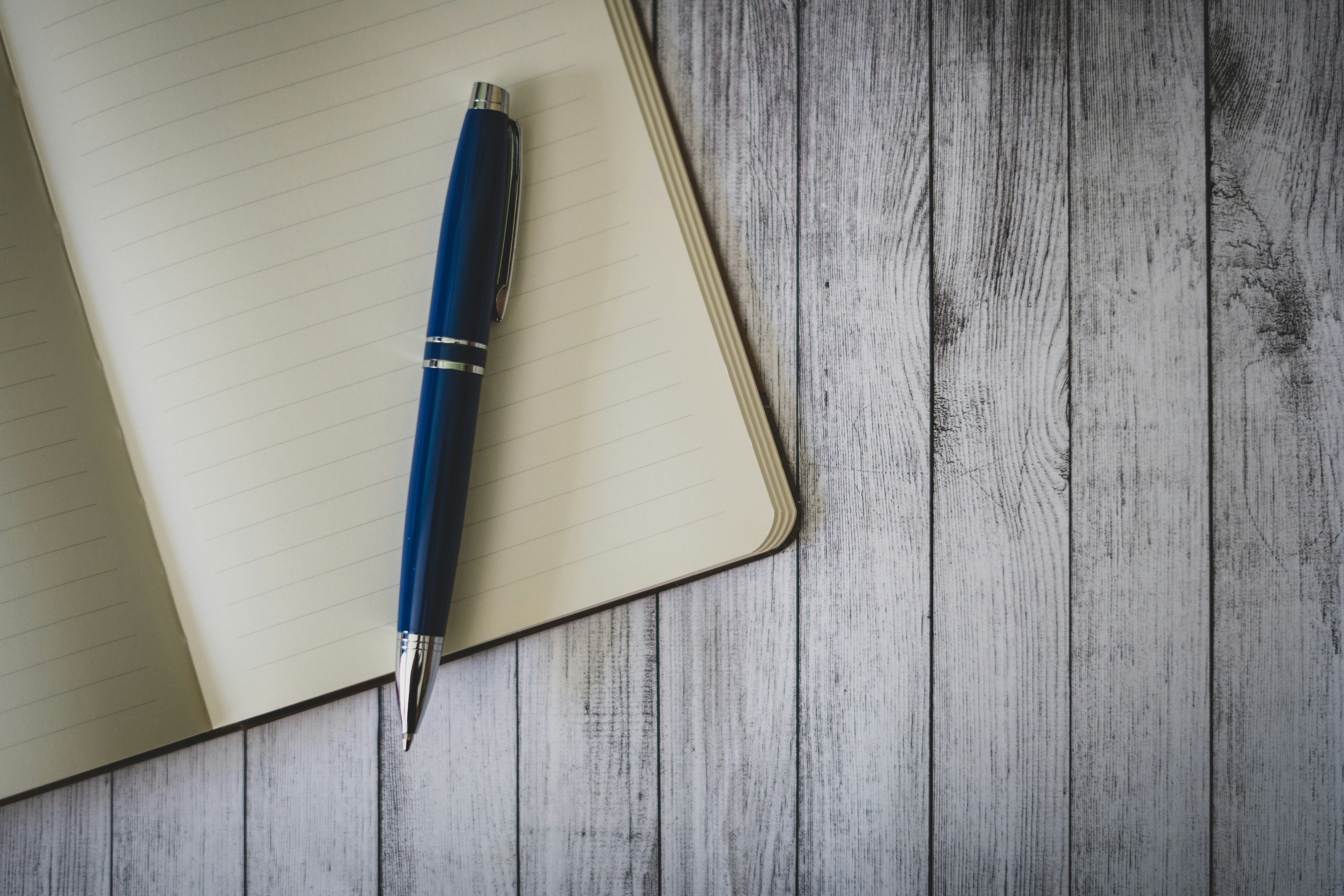 An open notebook with a pen resting on a blank lined page