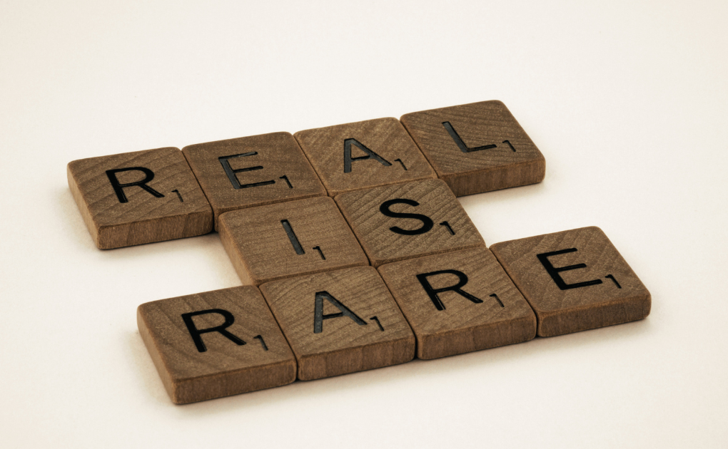 Scrabble tiles spelling REAL IS RARE on a white background